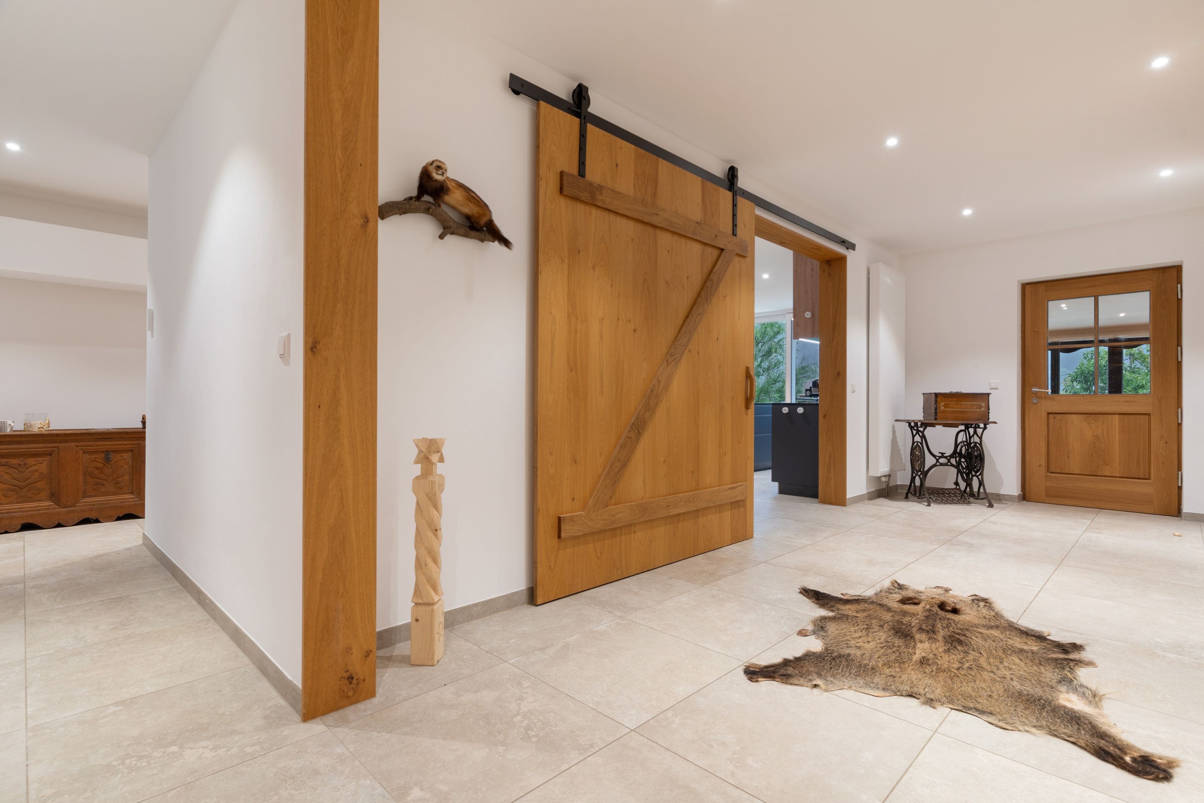 A spacious room with a large wooden sliding door, a rustic wooden sculpture, and a fur rug on the floor.