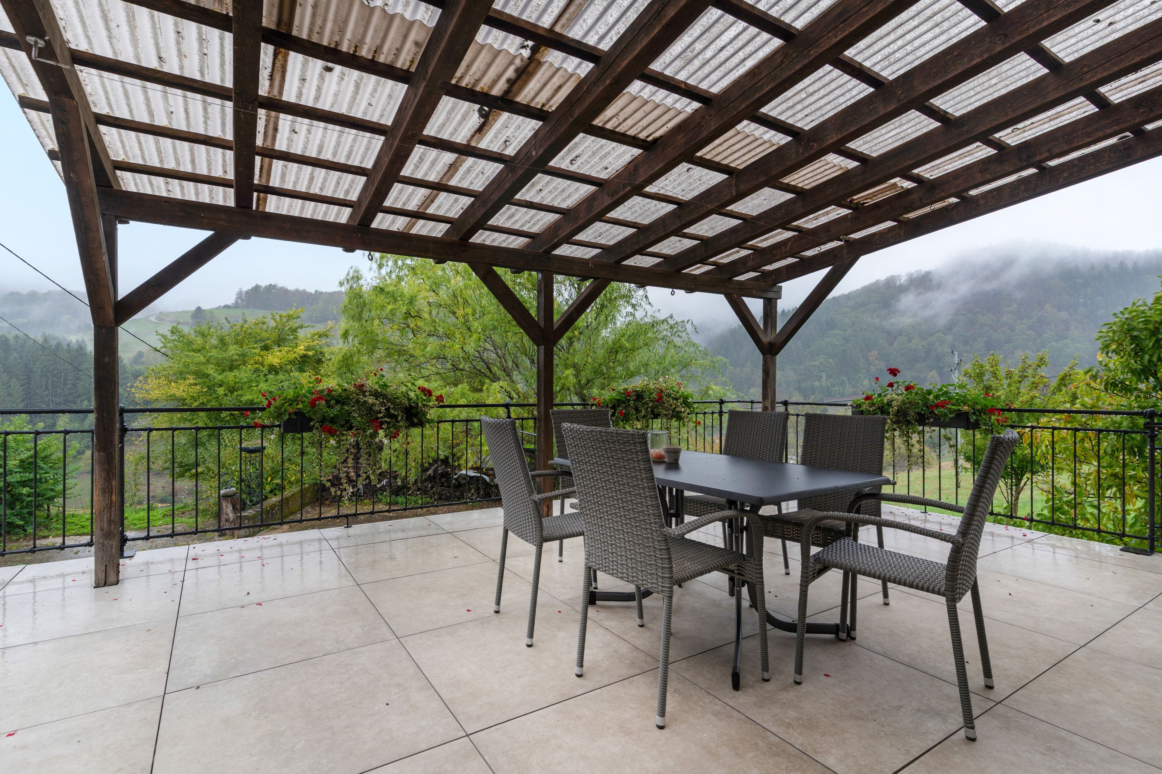 A covered patio with a table and chairs, surrounded by a metal railing and potted plants.