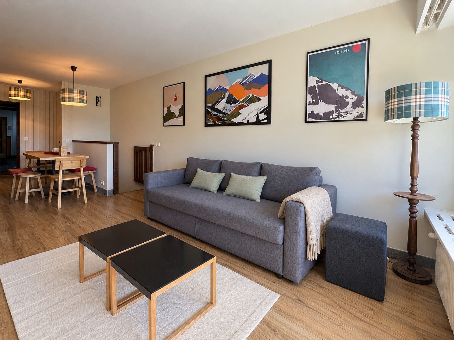 A modern living room with a grey sofa, wooden coffee table, and a dining area with a wooden table and chairs.