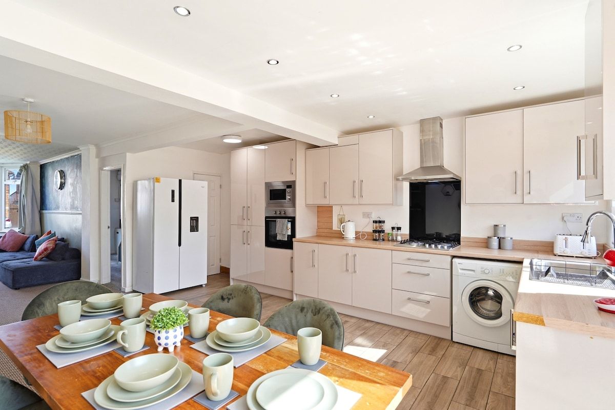Una cocina moderna con armarios blancos, una mesa de comedor de madera para cuatro comensales y una lavadora integrada.