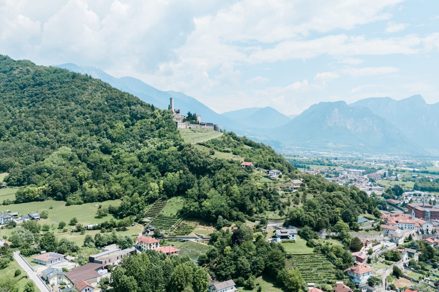 Un paysage montagneux avec un château perché sur une colline, entouré de verdure et surplombant une petite ville.