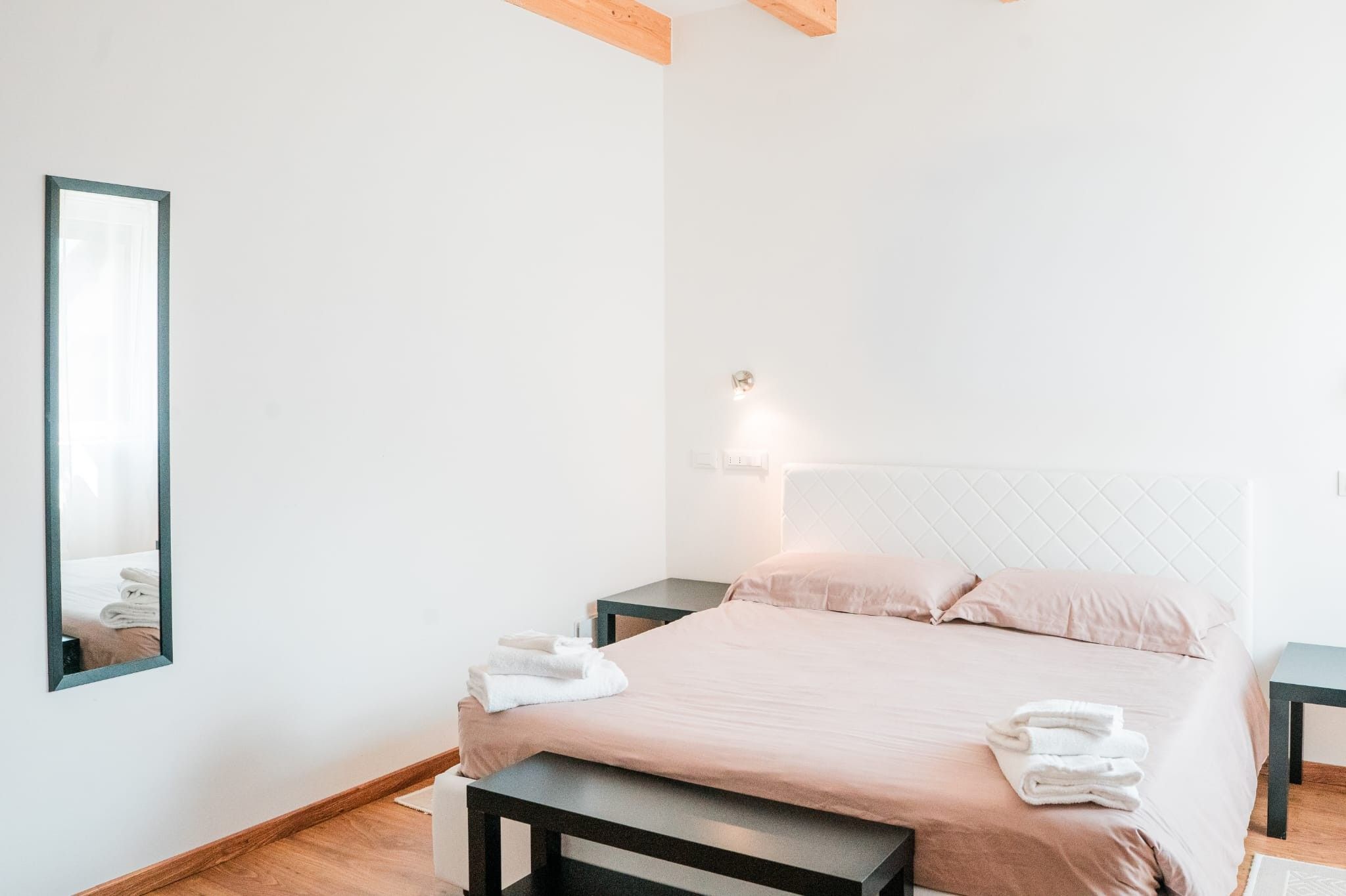Quarto de hotel com cama, mesas de cabeceira, espelho e luminária na parede.
