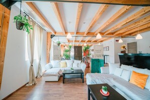 Uma sala de estar acolhedora com vigas de madeira, um sofá, uma mesa de centro e plantas penduradas.