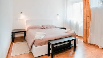 Une chambre à coucher avec un lit, des tables de chevet, un banc et une fenêtre avec des rideaux.