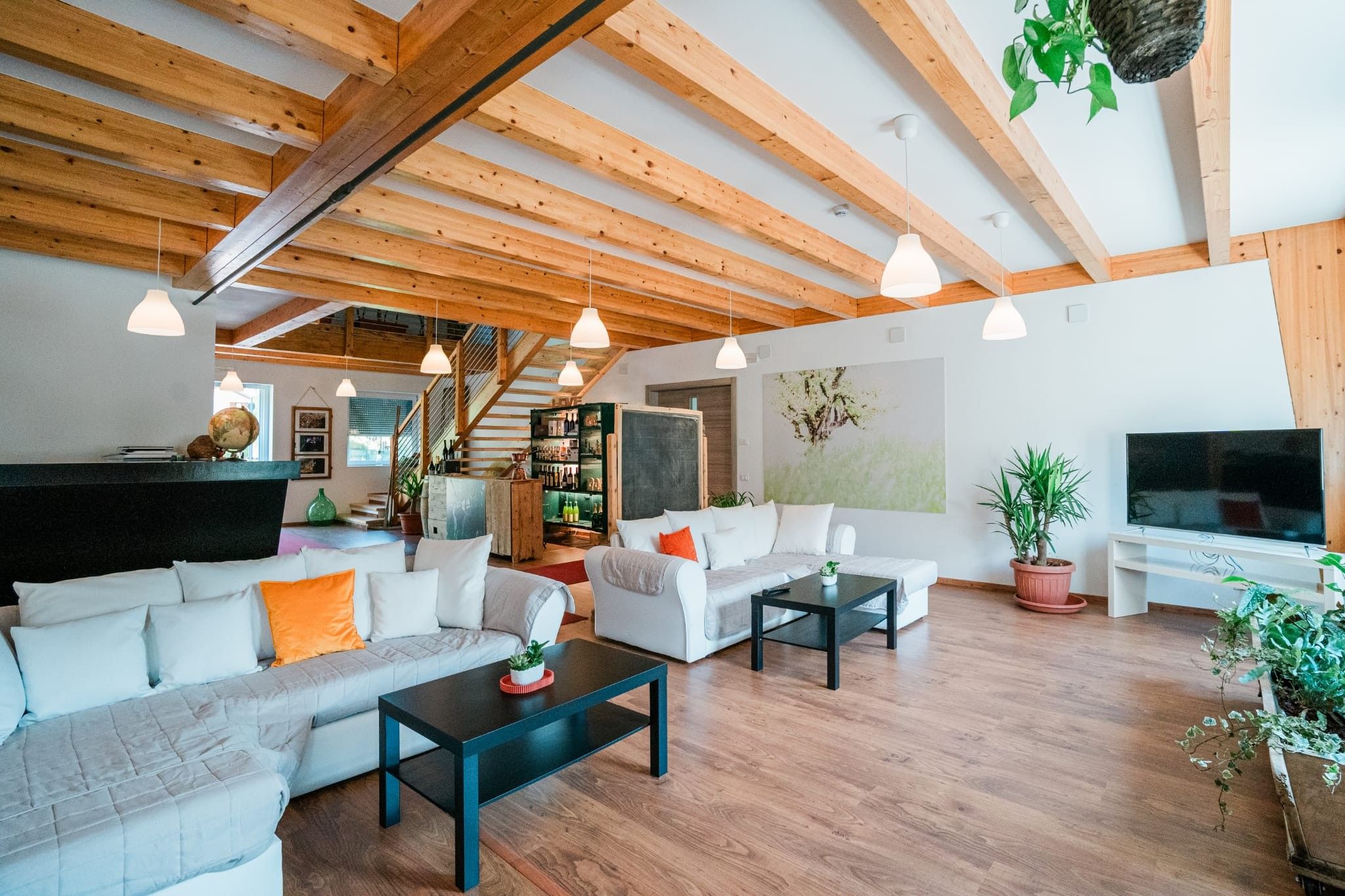 Un vaste espace de vie doté d’un plafond haut, de poutres en bois, d’un escalier, d’un coin bar et d’un téléviseur.