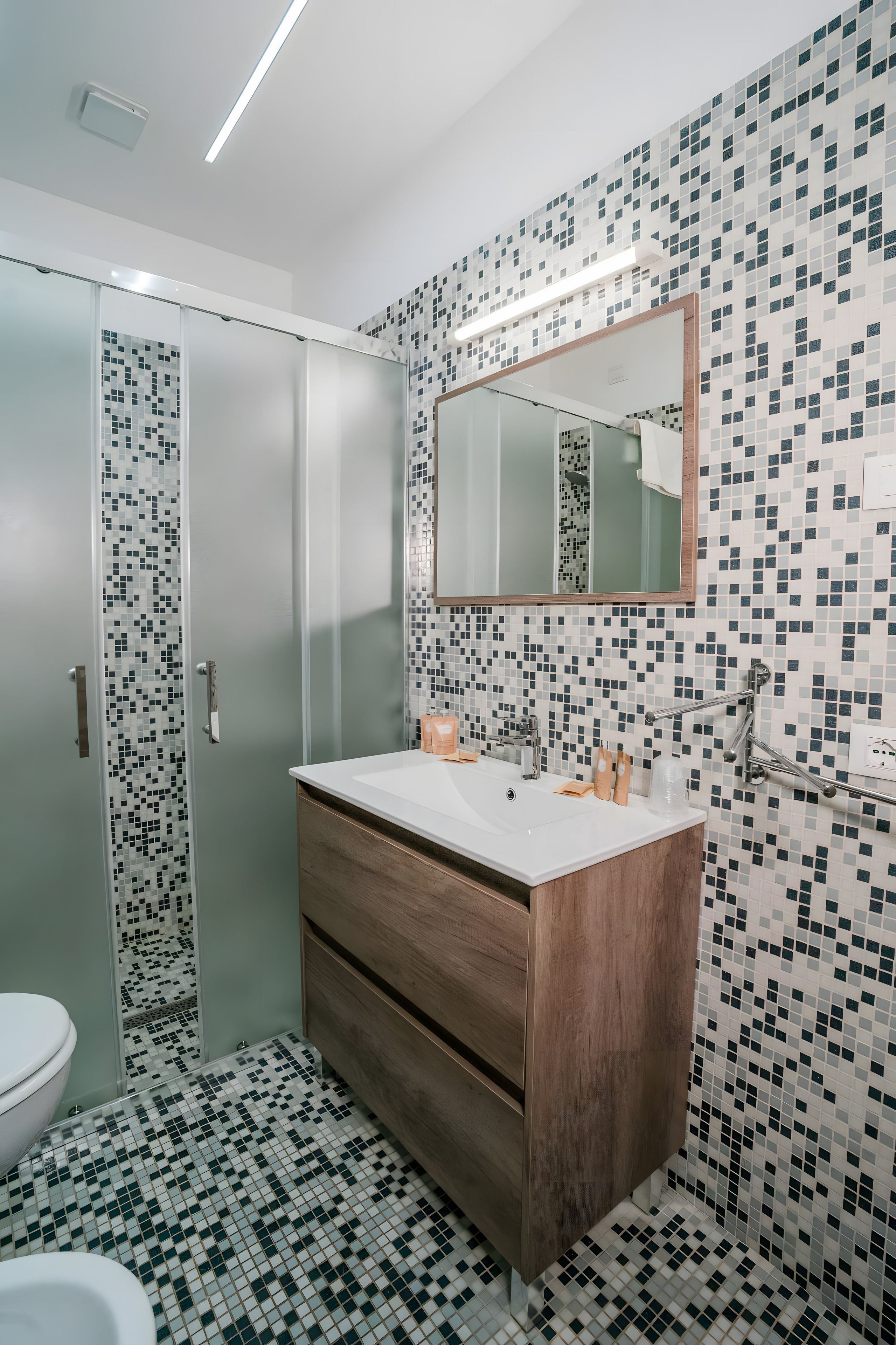 A bathroom with a glass shower enclosure, a wooden vanity, and a tiled backsplash.