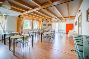 Un comedor espacioso con vigas de madera, varias mesas y sillas, y ventanas grandes que dejan entrar luz natural.