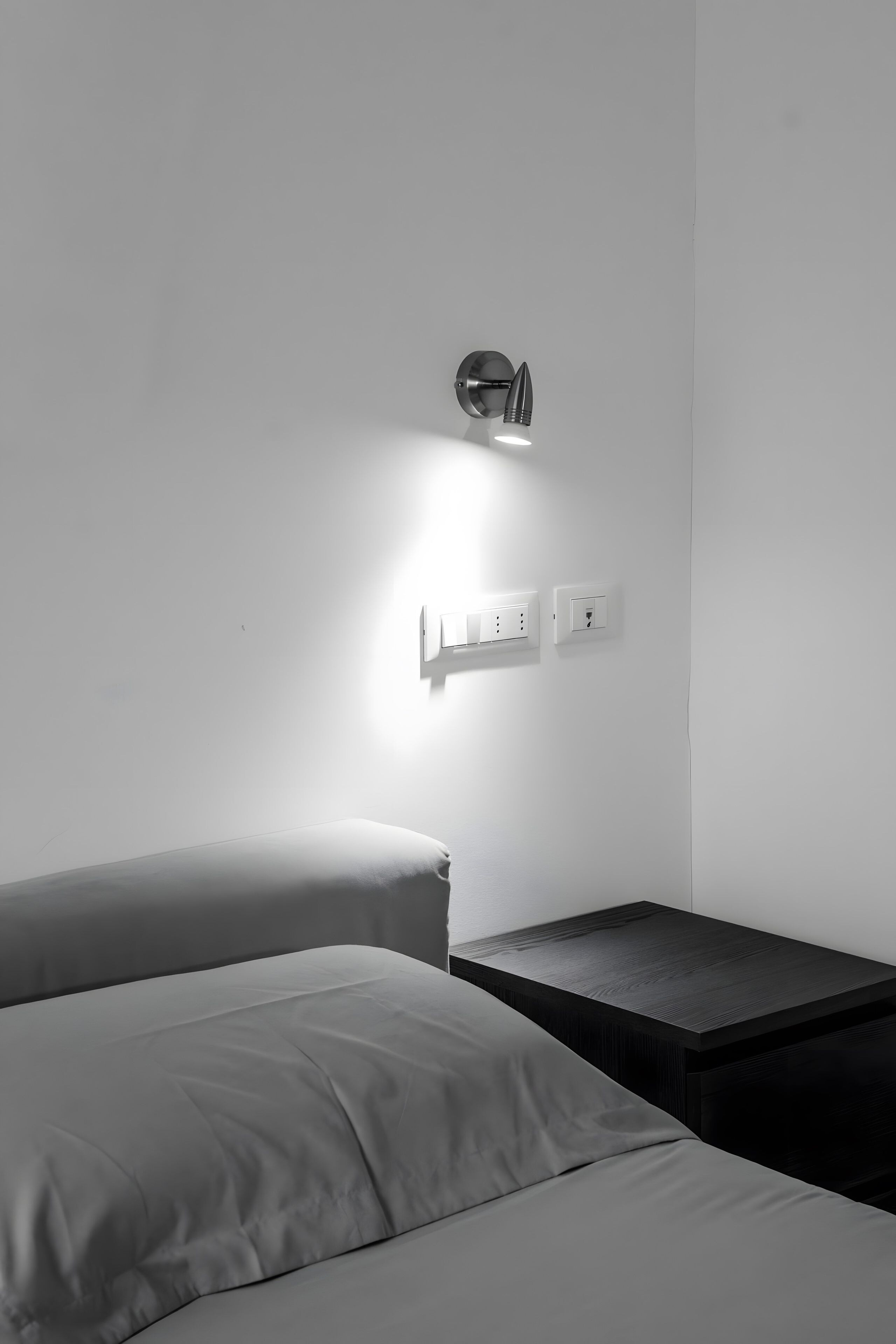 Habitació minimalista amb un llit, una tauleta de nit i una làmpada penjada a la paret.