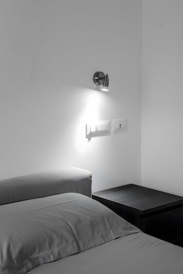 Una habitación minimalista con una cama, una mesita de noche y una lámpara de pared.