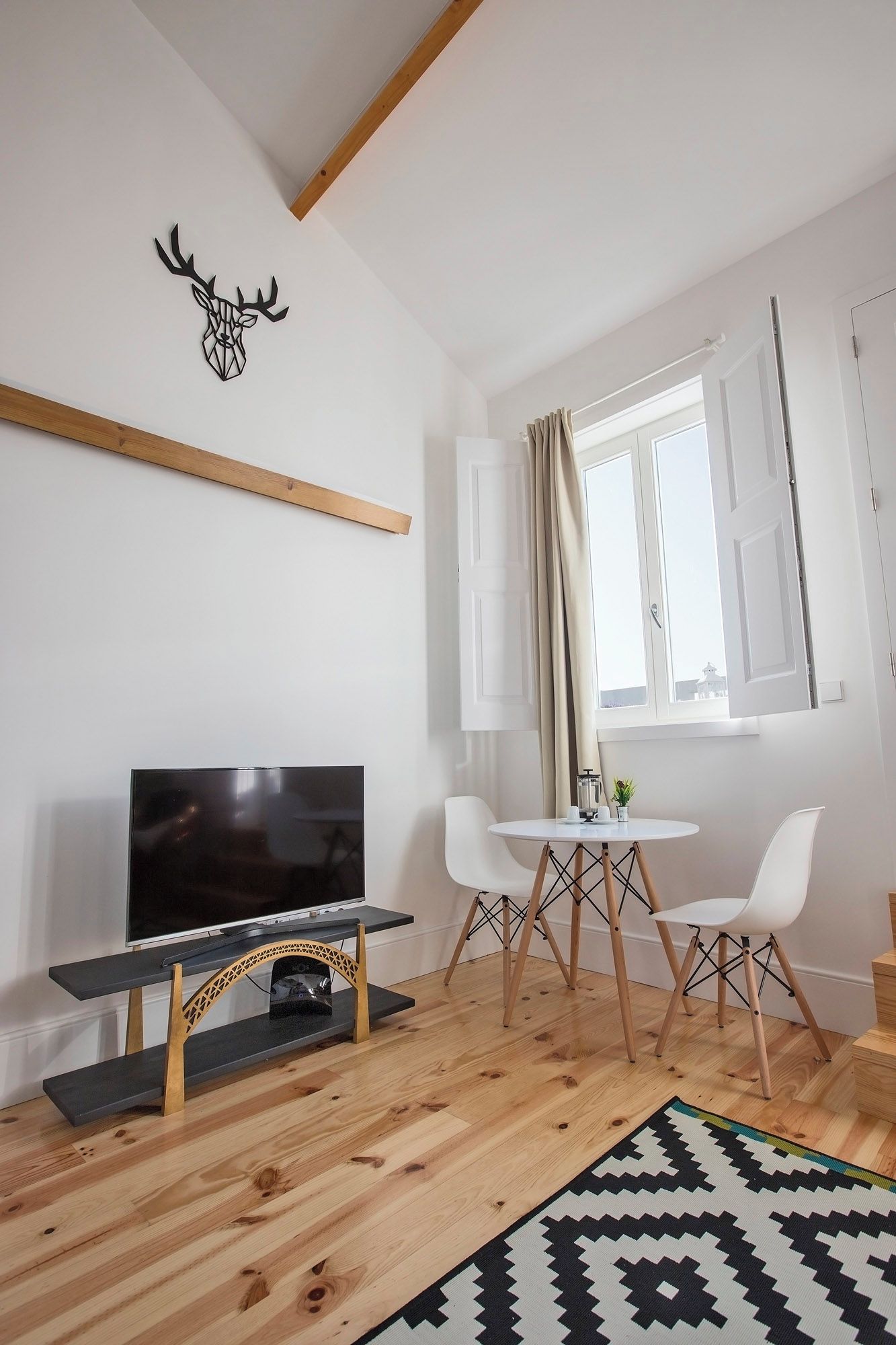 Ein modernes Wohnzimmer mit Flachbildfernseher, Holzboden, einem gemusterten Teppich und einem Essbereich mit kleinem Tisch und Stühlen.