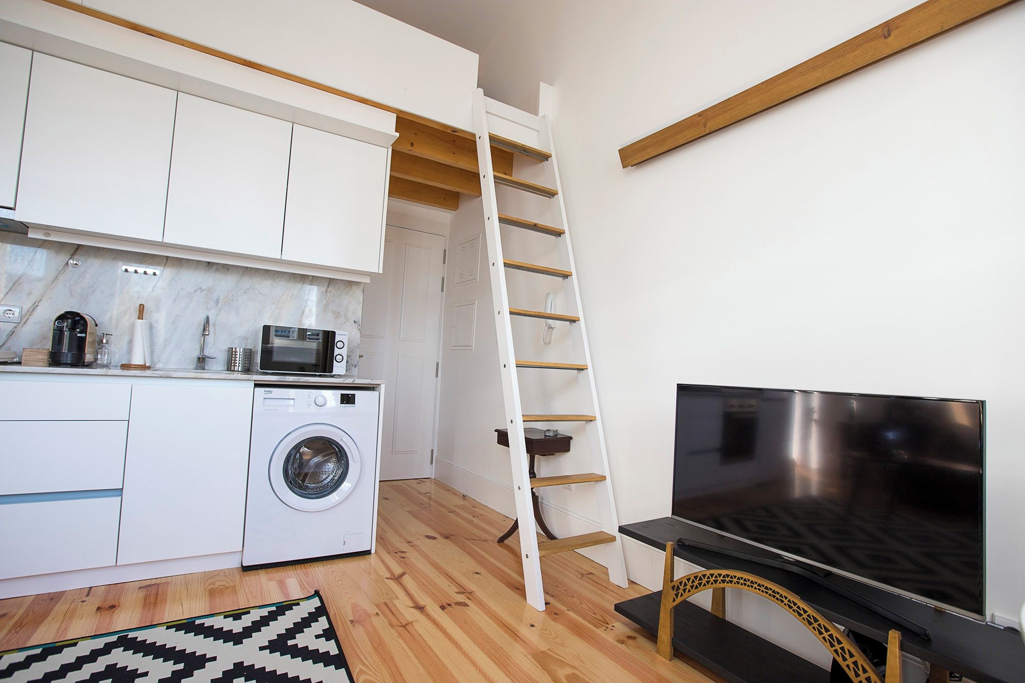 A compact kitchen with a washing machine, microwave, and a TV.