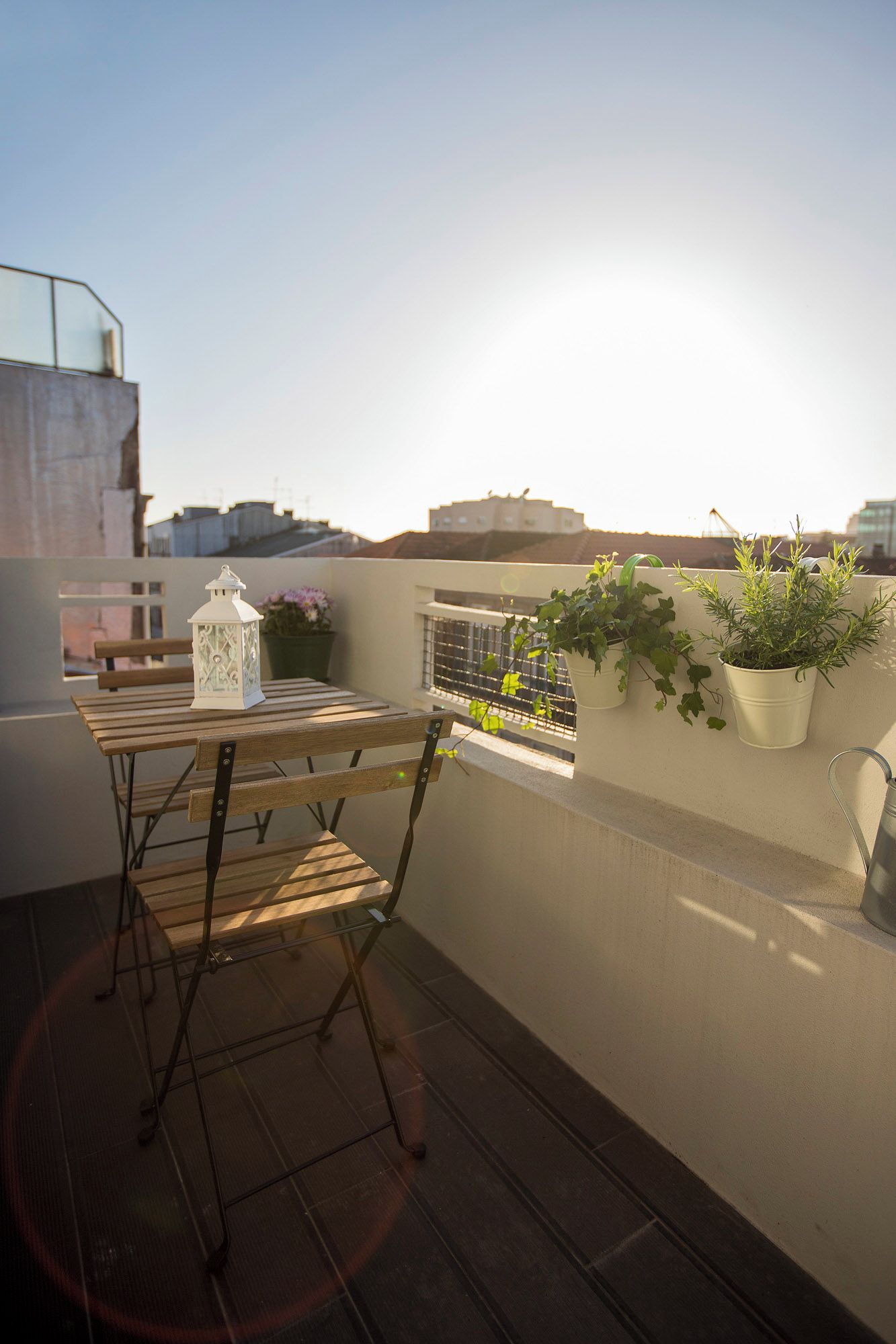 Eine Dachterrasse mit Holztisch und Stühlen, einem weißen Laternen und Kübelpflanzen.