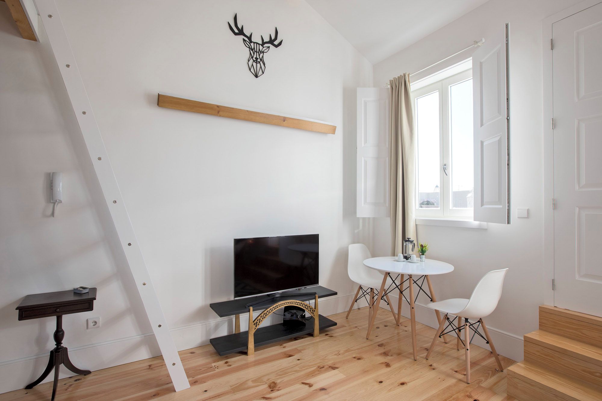 Una sala de estar moderna con televisor, piso de madera, una mesa de comedor con sillas, una cabeza de venado decorativa en la pared y una escalera que lleva a otra habitación.