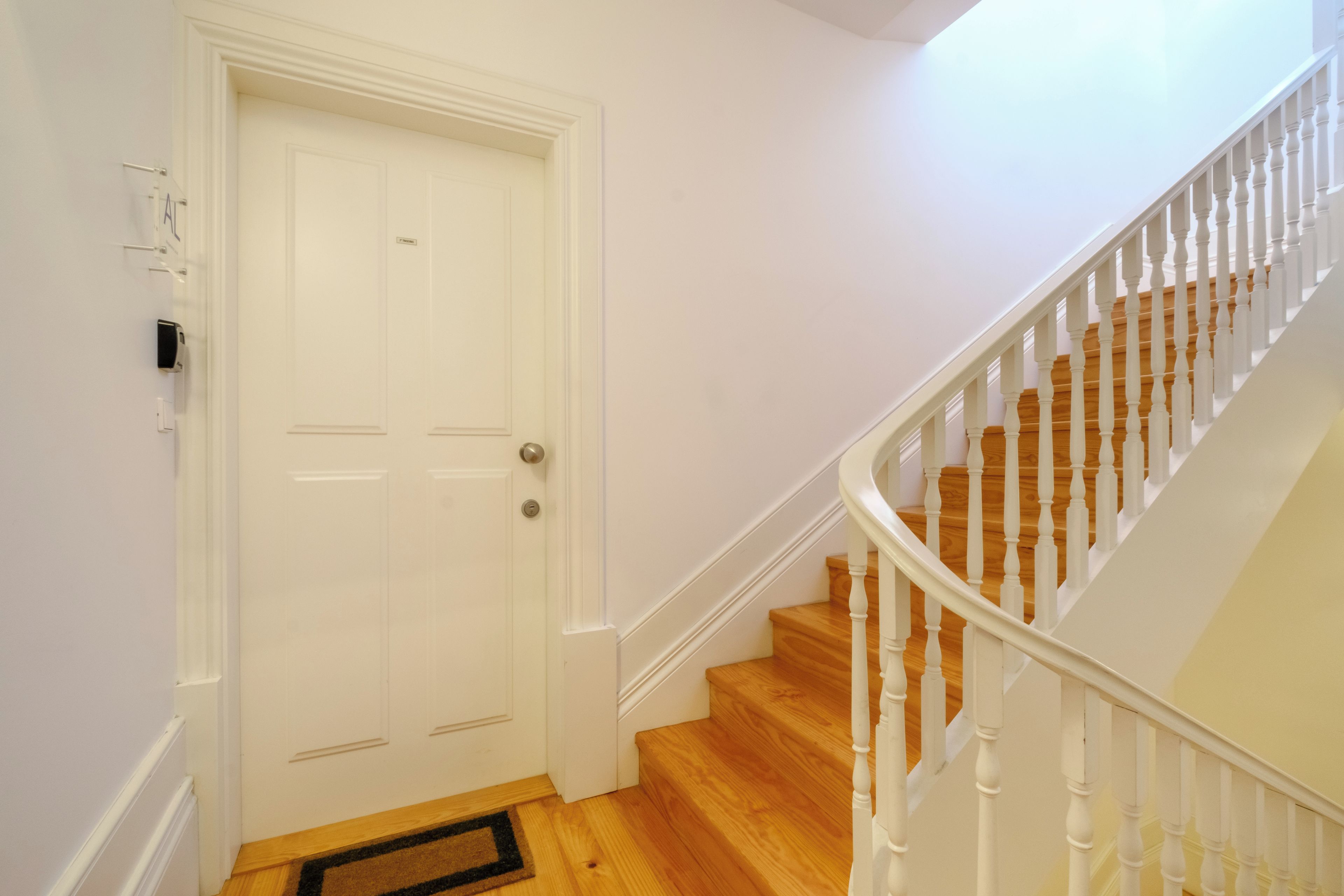 A staircase with white balusters and wooden steps leading to a white door with a doorknob and a small label.
