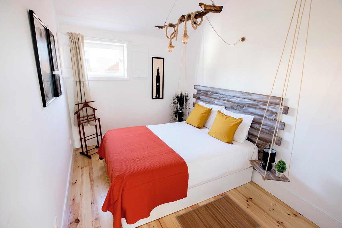 A bedroom with a bed, a wooden headboard, a red blanket, and a hanging light fixture.