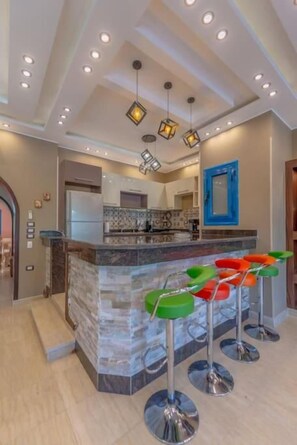 A modern kitchen with a marble island, bar stools, and pendant lighting.