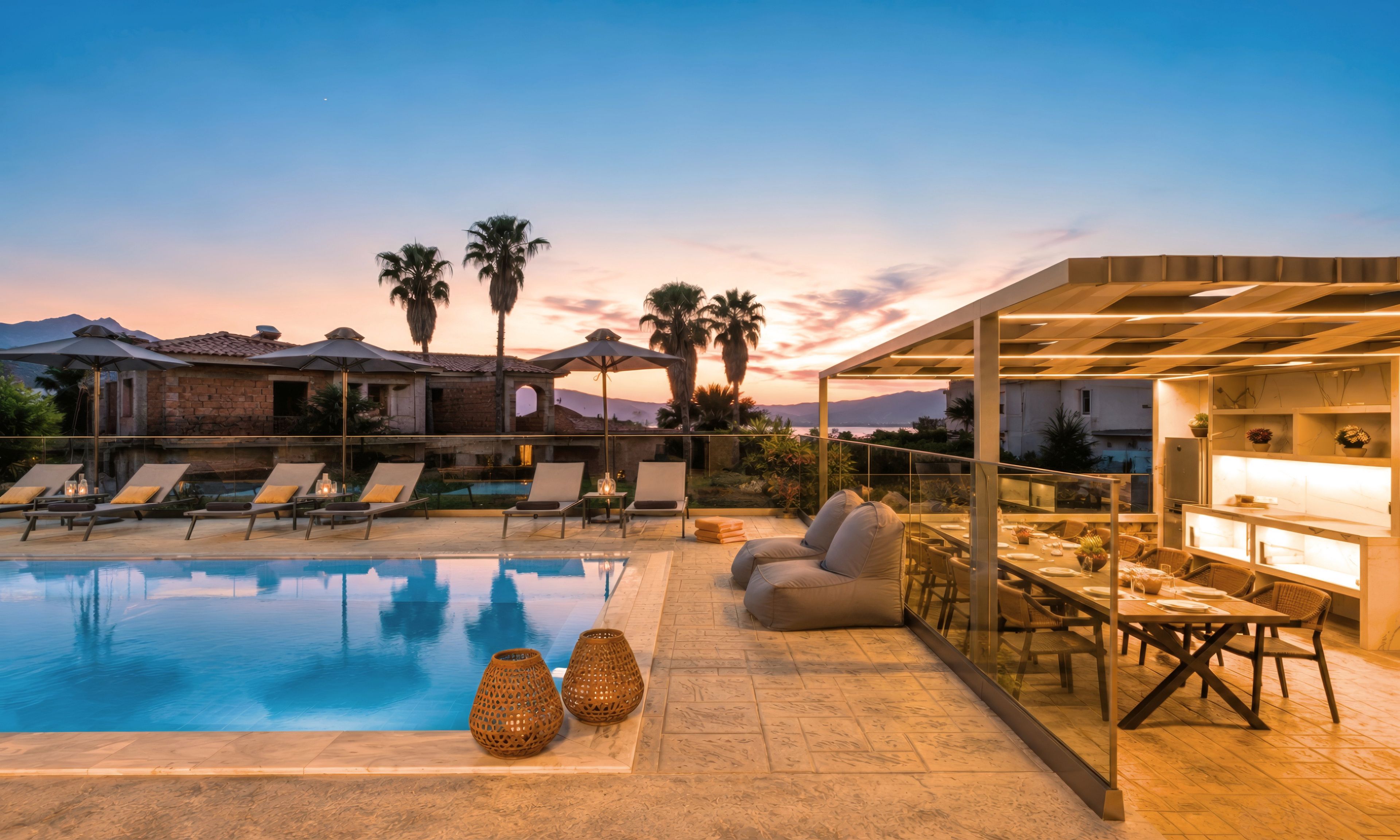 A poolside area with lounge chairs, a dining setup, and a view of mountains.