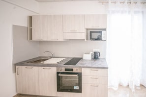 A compact kitchen with a sink, stove, microwave, and a small countertop area.