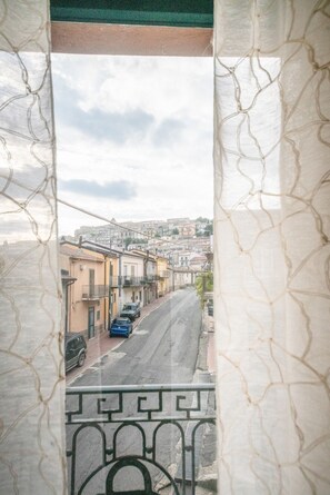 Un balcon donnant sur une rue bordée d’immeubles et de voitures garées.