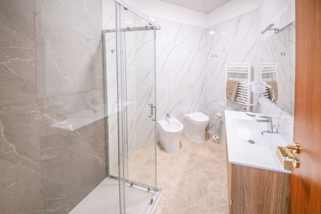 Un bagno moderno con cabina doccia in vetro, lavandino bianco e due servizi igienici.