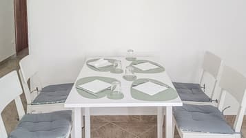 A dining area with a white table set for four, surrounded by white chairs with grey cushions.