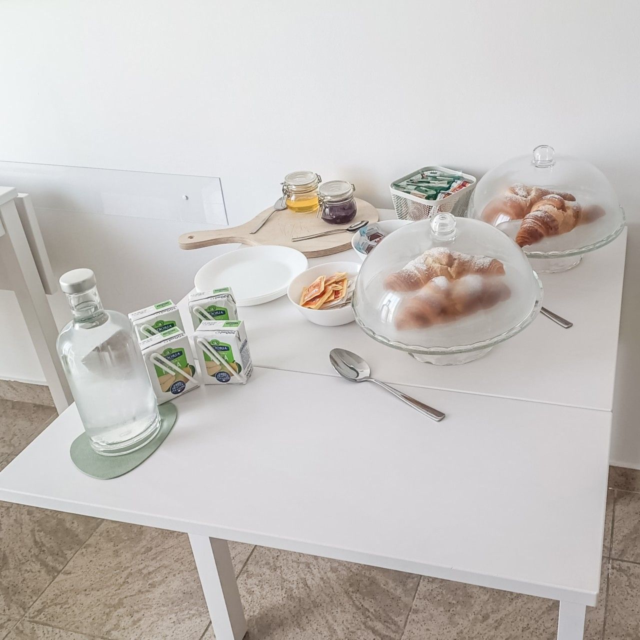 Una colazione servita su un tavolo di vetro, con una bottiglia, cibo confezionato e un piatto coperto di pasticceria.