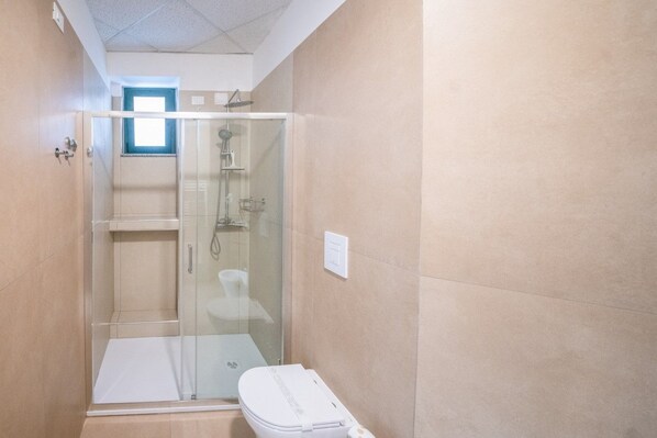 A bathroom with a glass-enclosed shower, a toilet, and a small window.