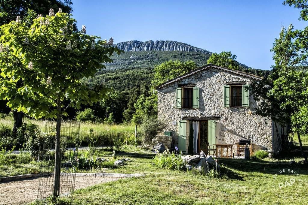 Una casa de piedra con puerta y ventanas, rodeada de vegetación y una montaña al fondo.