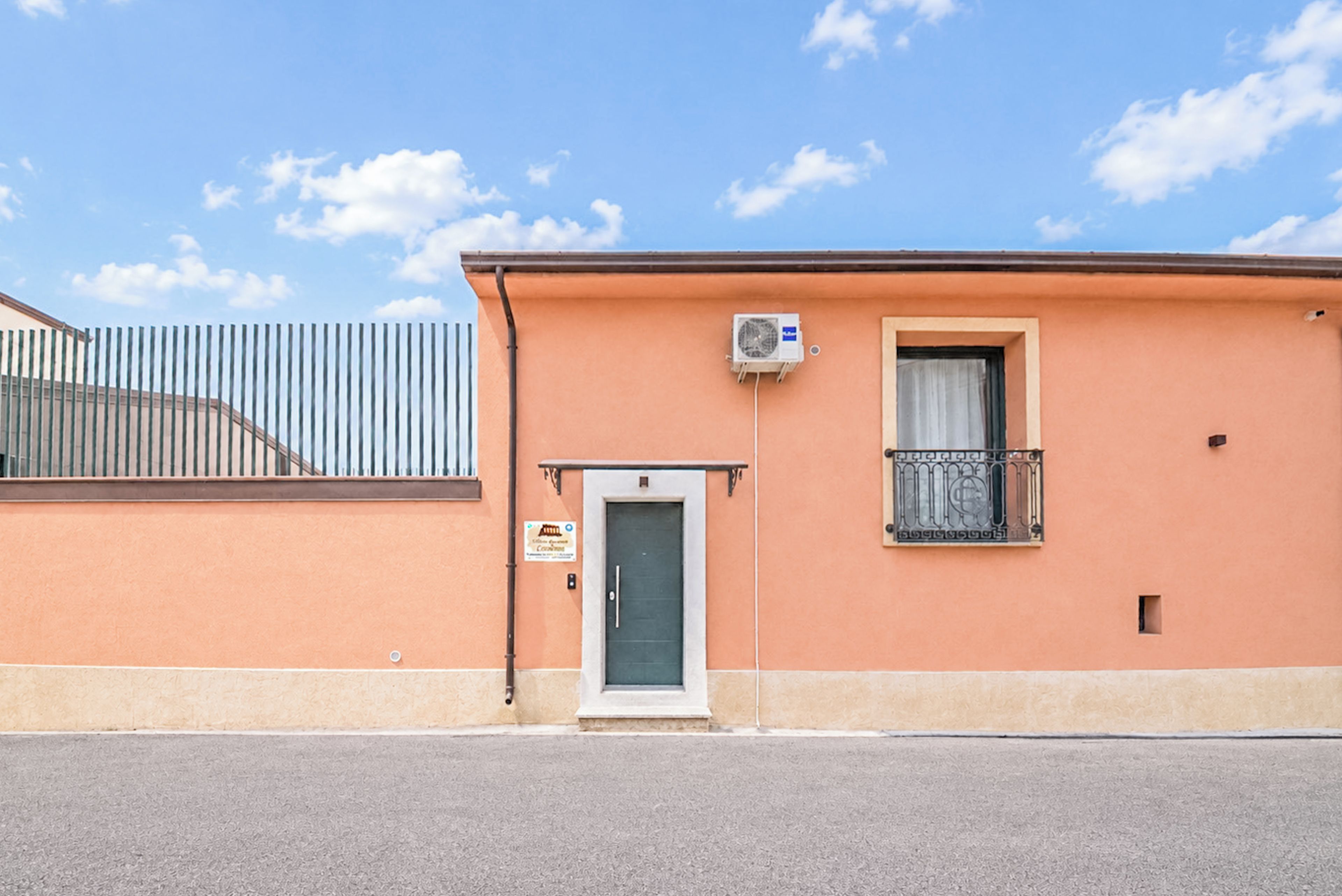 A building with a single door, a small window with a metal grille, and an air conditioning unit mounted on the wall.