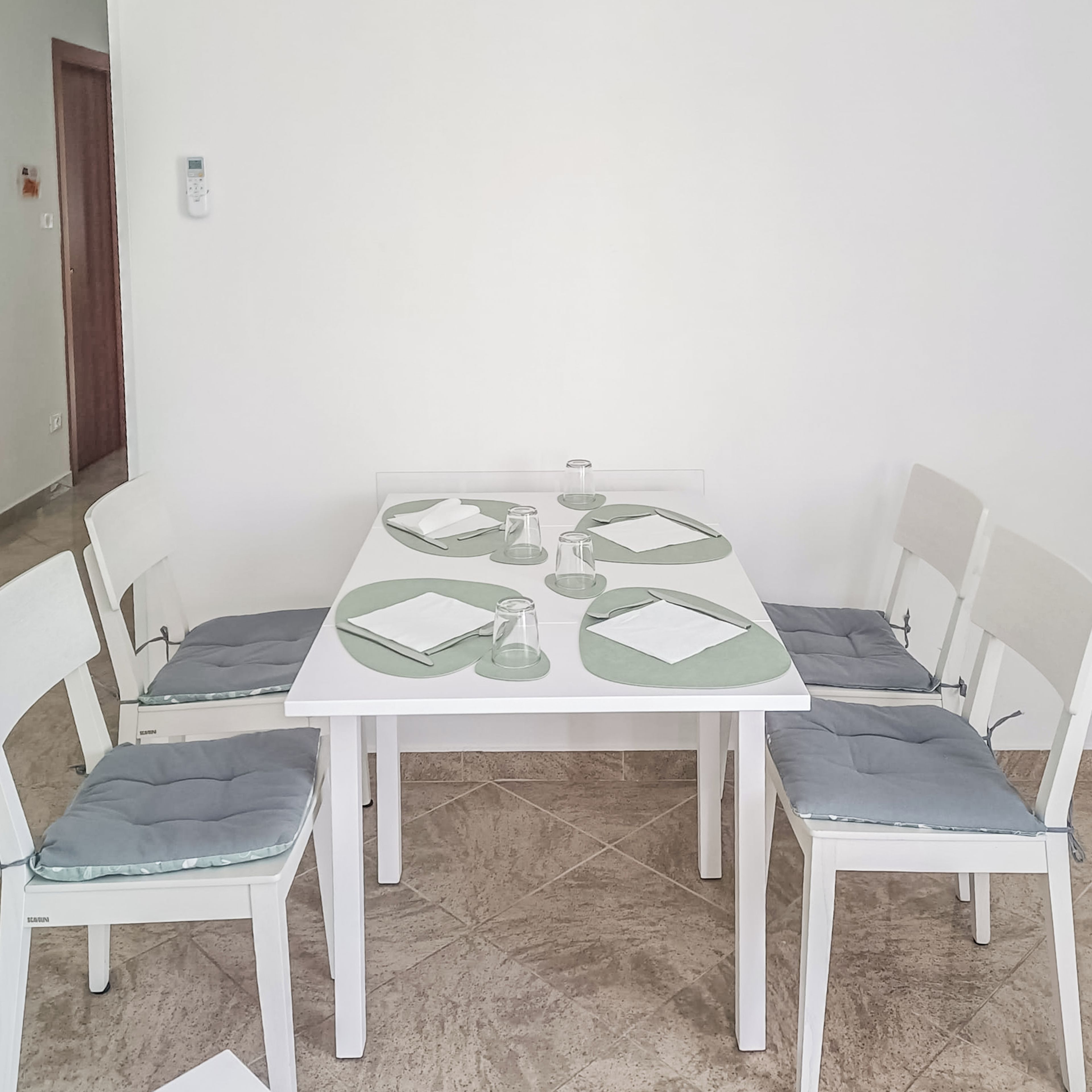Una mesa de comedor con cuatro sillas, cada una con un cojín. La mesa está preparada con platos, vasos y cubiertos.