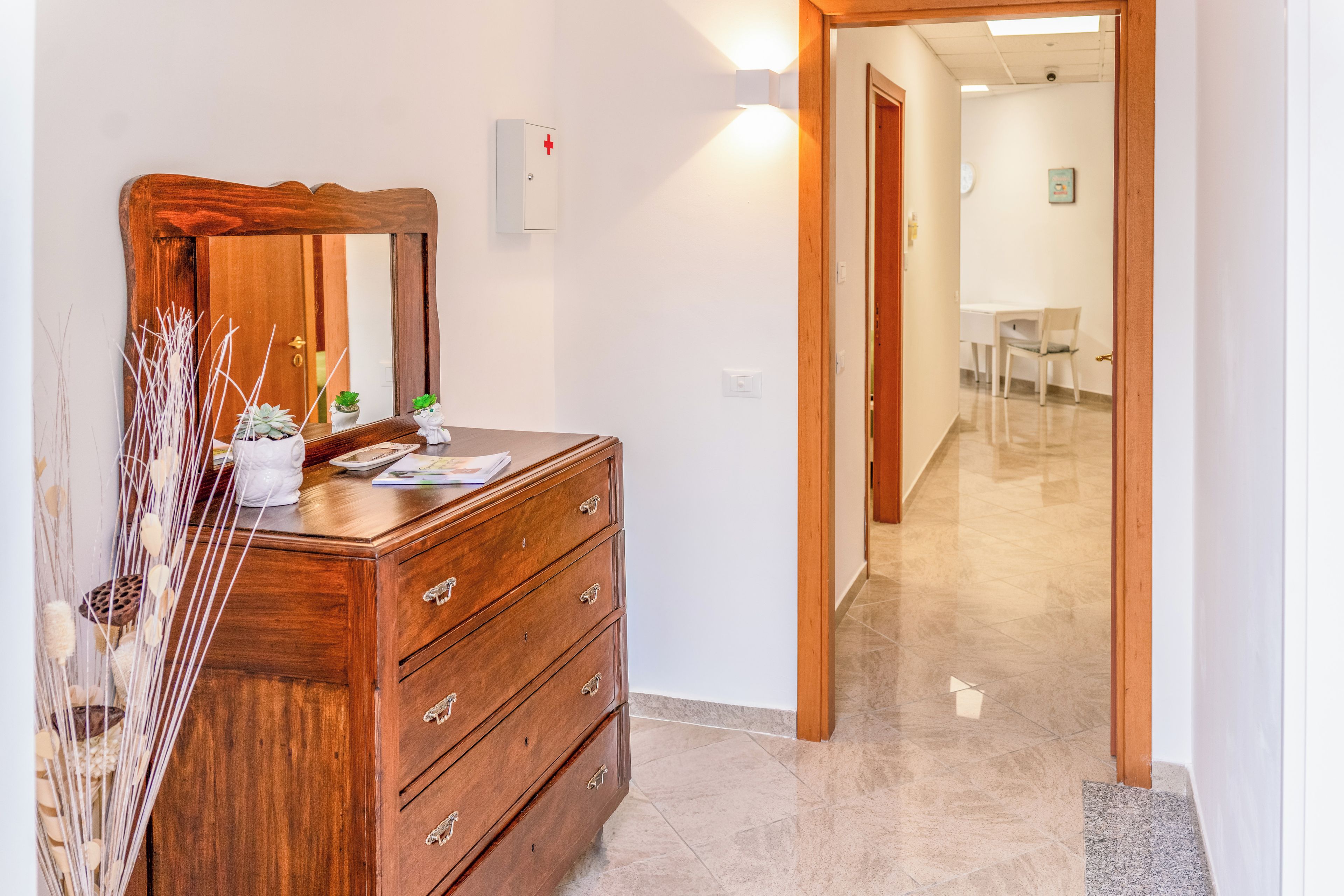A wooden dresser with drawers and a mirror, a wall-mounted light, and a door leading to a hallway.