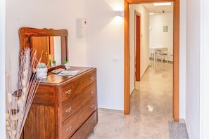 A wooden dresser with drawers and a mirror, a wall-mounted light, and a door leading to a hallway. - Holiday Apartment Levidonia (Albidona)