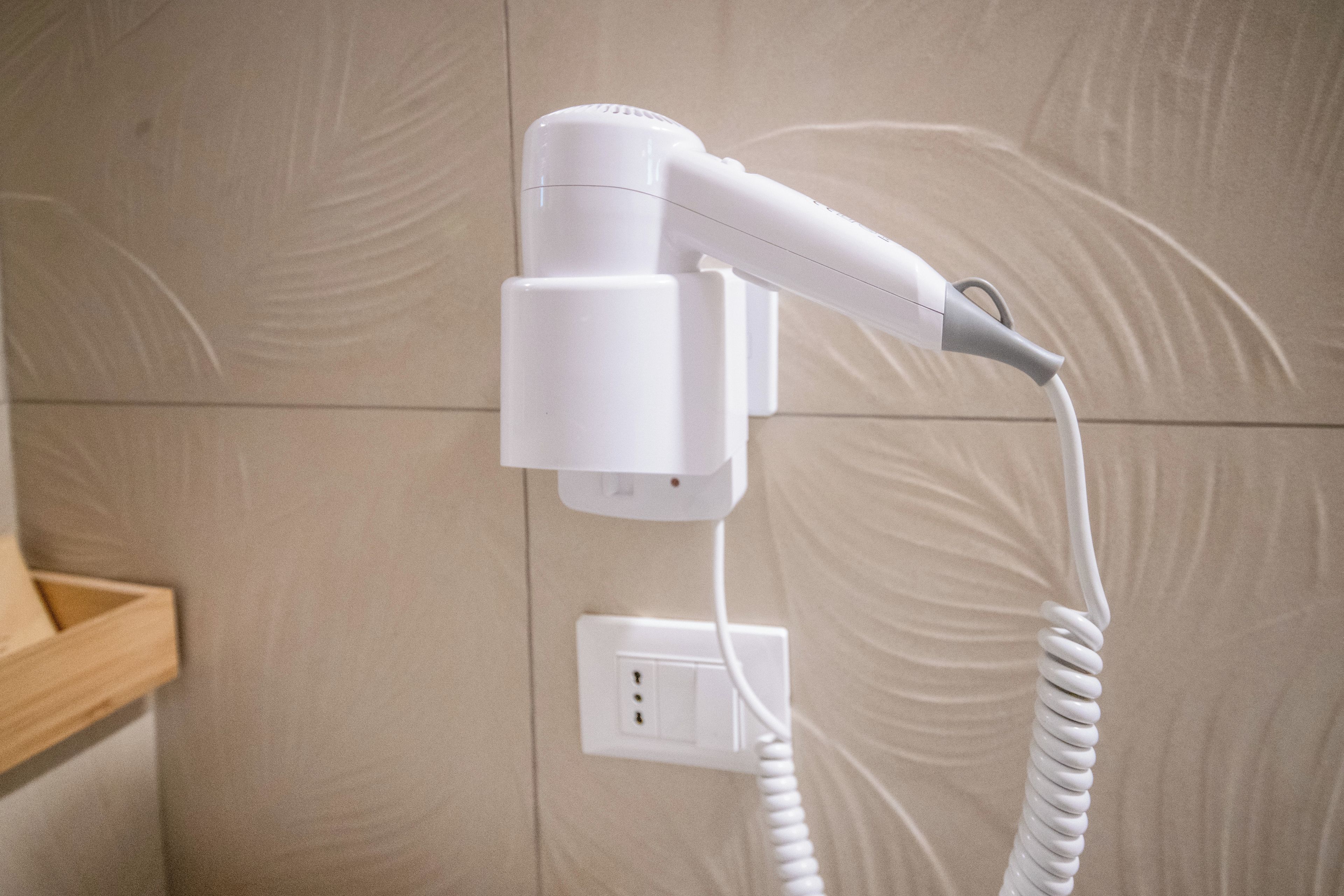 Un asciugacapelli bianco fissato al muro con il cavo arrotolato.