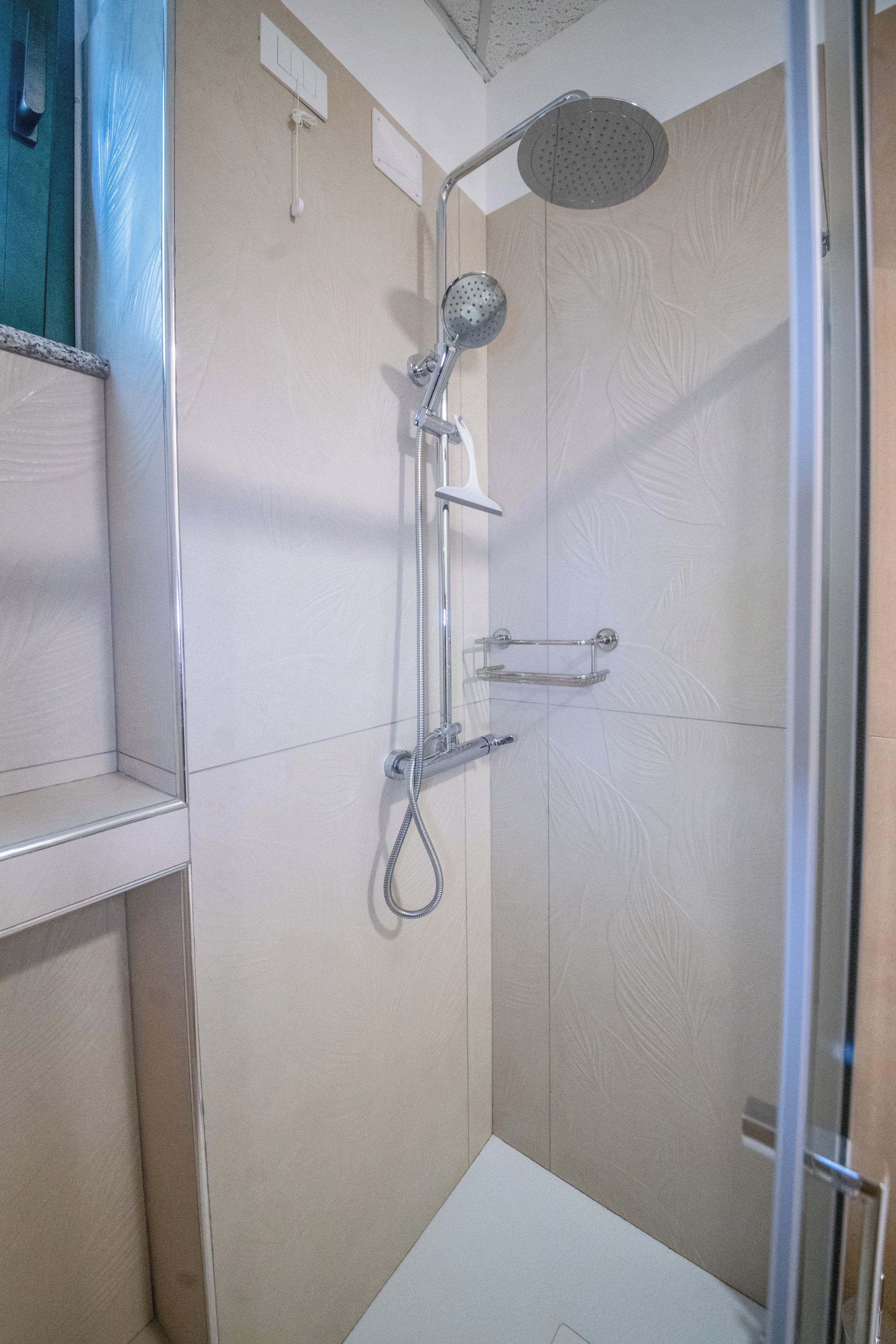 Ducha con cabezal de ducha de mano, panel de control en la pared y puerta de cristal.