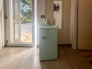 A compact room with a door leading to an outdoor area, a small refrigerator, and a wall-mounted light fixture. - Fiordo Rooms - Paradise Rooms (Ripabottoni)