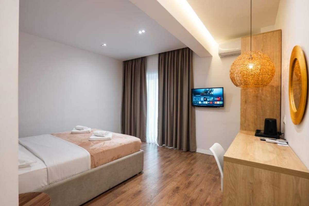 Una camera d'albergo moderna con un letto, una scrivania, una televisione e un'ampia finestra con tende.