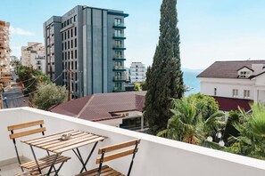 Un balcone con tavolo e sedie in legno, affacciato su una vista urbana con edifici e un corpo d'acqua.