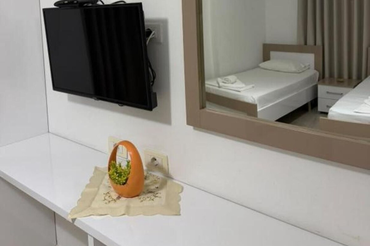 Una camera d'albergo con un letto, un comodino, uno specchio e una TV a parete.