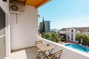 A balcony with a pool, a table, and chairs, overlooking a pool area and buildings. - Andrea Boutique Hotel (Sarande)