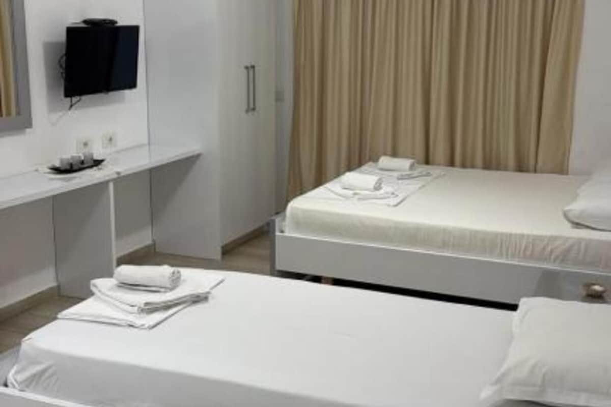 Una camera d'albergo con due letti, una scrivania, una televisione e un condizionatore.