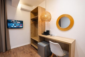 A hotel room with a television displaying a sports channel, a wooden desk with a coffee maker, a compact refrigerator, and a white chair. - Andrea Boutique Hotel (Sarande)