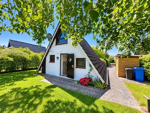 Een wit huis met een schuin dak, een voordeur en een kleine tuin met rode bloemen.