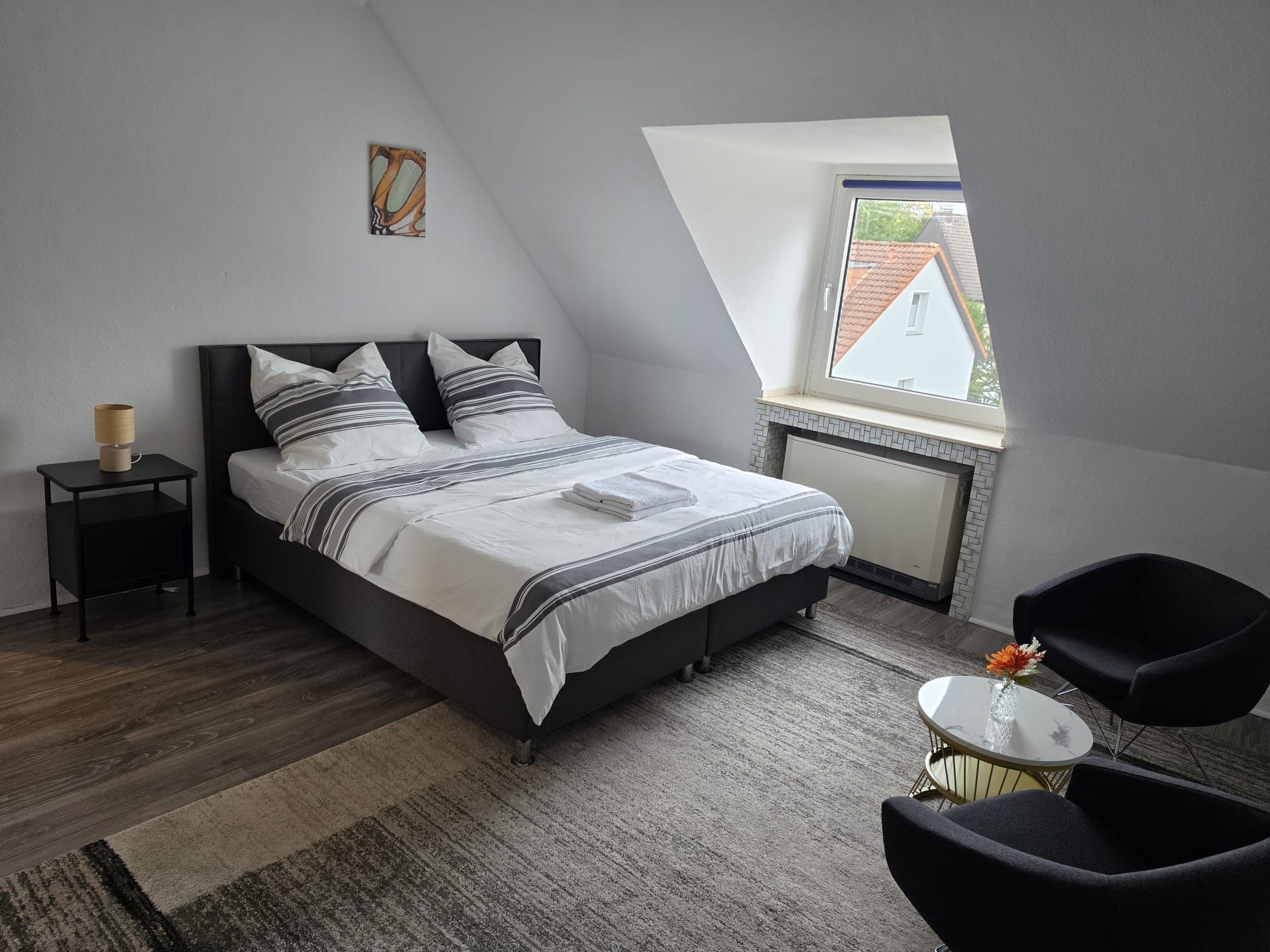 A bedroom with a bed, a nightstand, a chair, a small table, and a window.