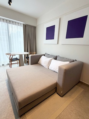 A modern hotel room with a sofa bed, a small table, and chairs. There are two framed artworks on the wall. - Modern Condesa loft with a king bed, full kitchen and fast Wi-Fi. Shared rooftop with views of Chapultepec Castle and forest, 24/7 security and self check-in. Walk to Parque México and the best cafés in town. (Hipódromo Condesa)