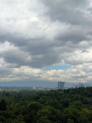 A cityscape with dense green foliage in the foreground and a skyline of buildings in the background under a cloudy sky. - Modern Condesa loft with a king bed, full kitchen and fast Wi-Fi. Shared rooftop with views of Chapultepec Castle and forest, 24/7 security and self check-in. Walk to Parque México and the best cafés in town. (Hipódromo Condesa)