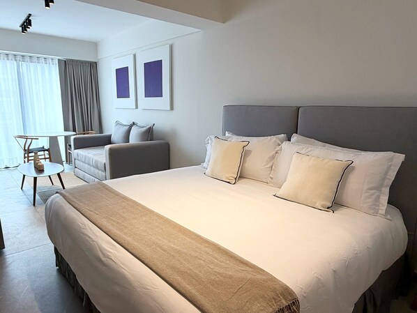 Ett hotellrum med en stor säng, ett litet bord, en soffa och en stol. Det finns två inramade tavlor på väggen.