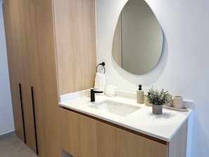 A bathroom with a wooden cabinet, a sink, a mirror, a towel, a soap dispenser, and a potted plant. - Modern Condesa loft with a king bed, full kitchen and fast Wi-Fi. Shared rooftop with views of Chapultepec Castle and forest, 24/7 security and self check-in. Walk to Parque México and the best cafés in town. (Hipódromo Condesa)