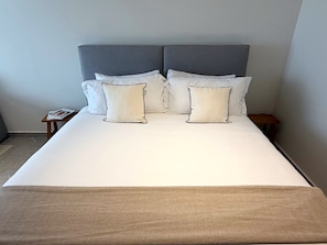 A bed with a grey upholstered headboard, white bedding, and two bedside tables with a magazine on one. - Modern Condesa loft with a king bed, full kitchen and fast Wi-Fi. Shared rooftop with views of Chapultepec Castle and forest, 24/7 security and self check-in. Walk to Parque México and the best cafés in town. (Hipódromo Condesa)