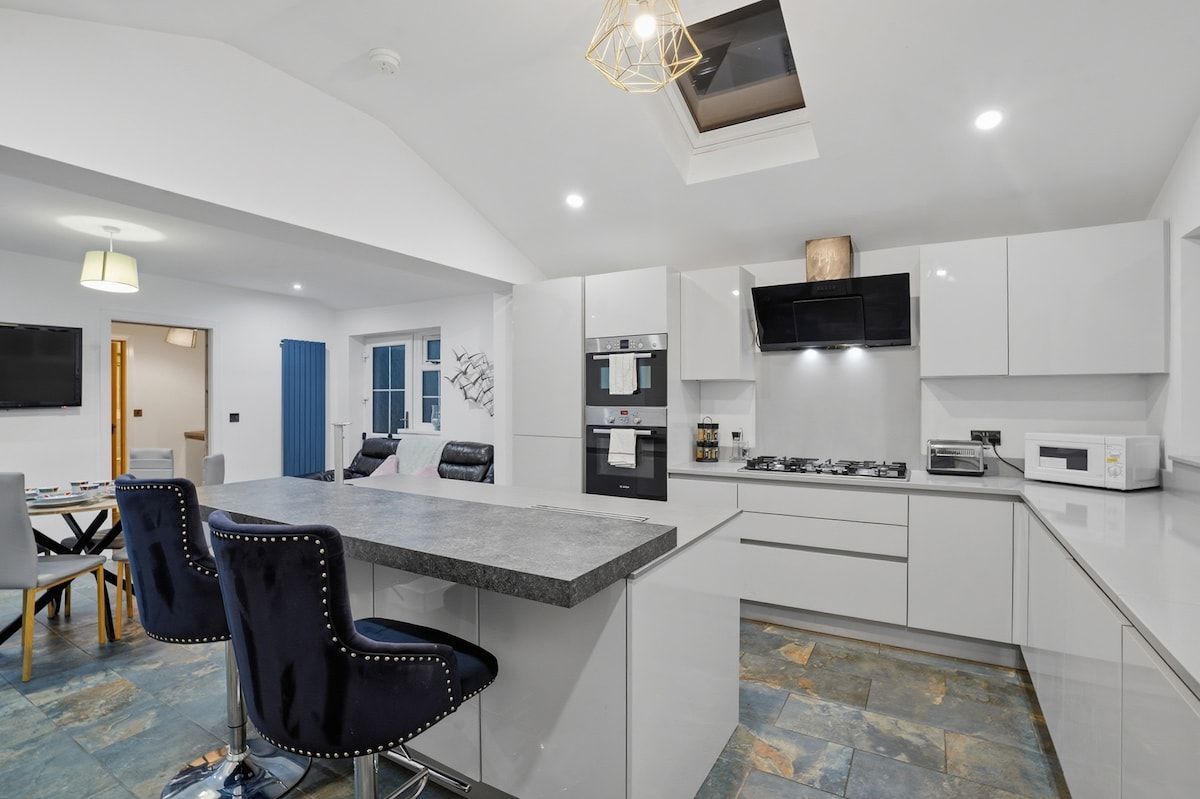 A modern kitchen with white cabinetry, a central island, and a dining area with chairs.