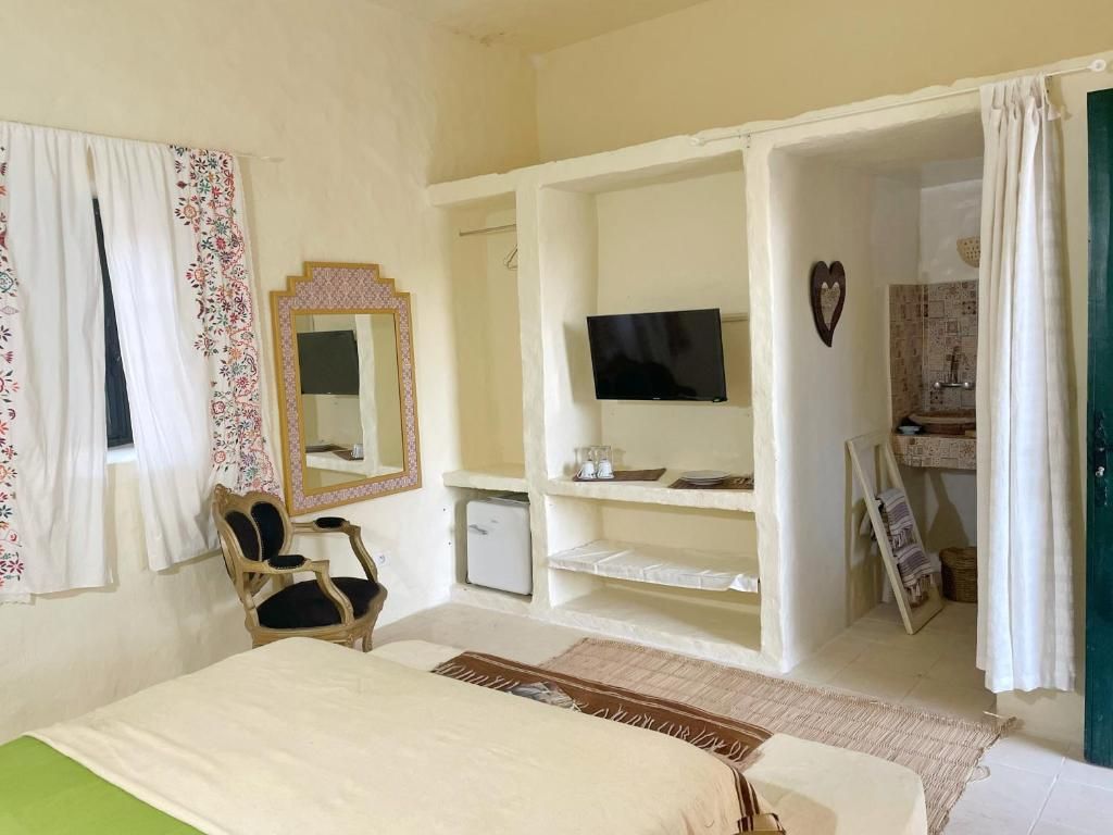 A bedroom with a bed, a chair, a television, a mirror, and a small cabinet.